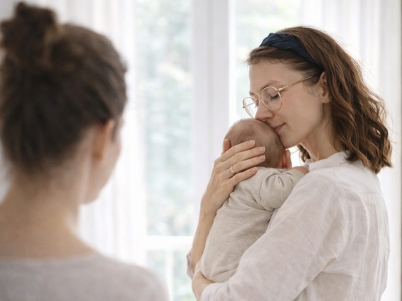 Mutter hält ihr Baby geborgen im Arm, eine zweite Frau ist bei ihr